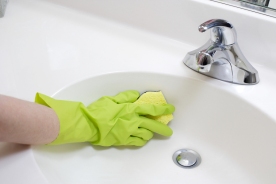 A person cleaning the bathroom sink with a glove